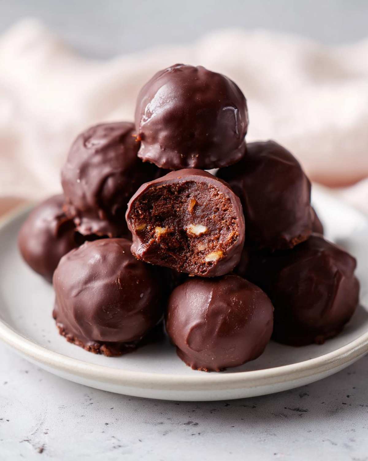 A stack of decadent, chocolate-coated pecan pie balls, with one bitten to show the nutty interior.