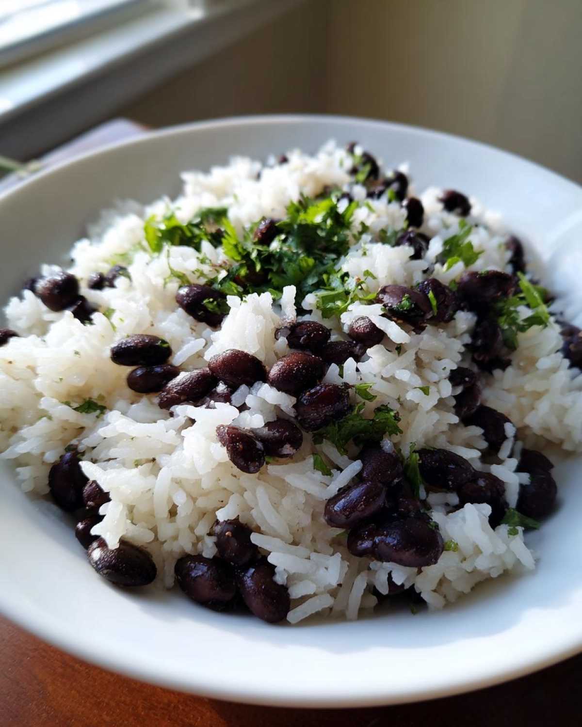 Close-up of fluffy white rice mixed with dark black beans and topped with fresh chopped cilantro.