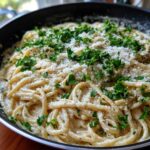 Close-up of creamy parmesan pasta tossed in a skillet, topped with grated cheese and fresh parsley.