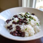 A white bowl filled with fluffy white rice topped generously with dark black beans and chopped fresh cilantro.