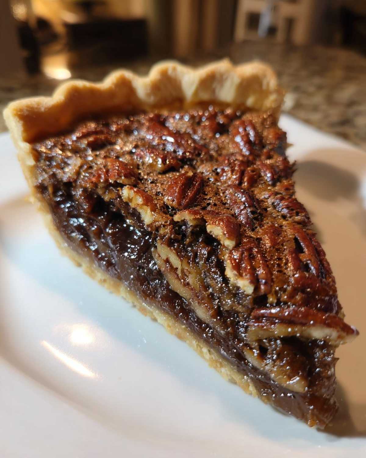 A close-up, angled shot of a perfect slice of chocolate pecan pie on a white plate.
