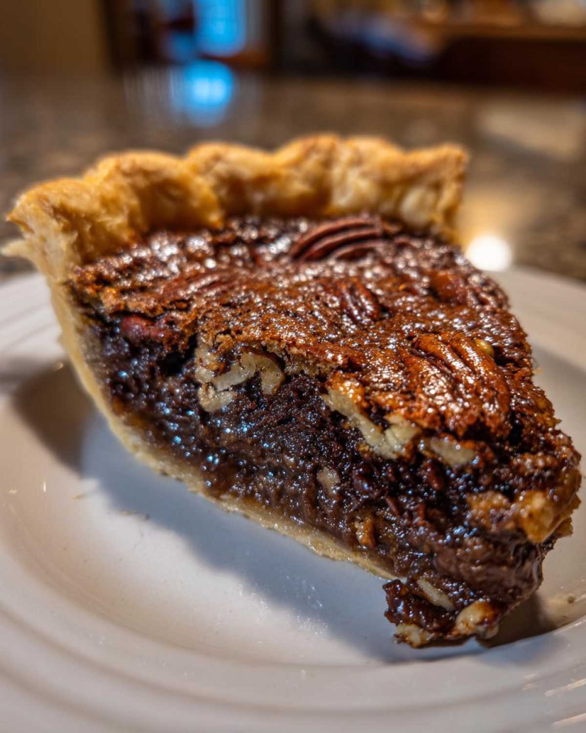 A close-up of a decadent slice of chocolate pecan pie showing the gooey filling and pecans on a white plate.