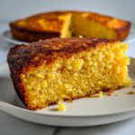 A close-up slice of golden yellow skillet cornbread showing a moist crumb and dark caramelized crust.