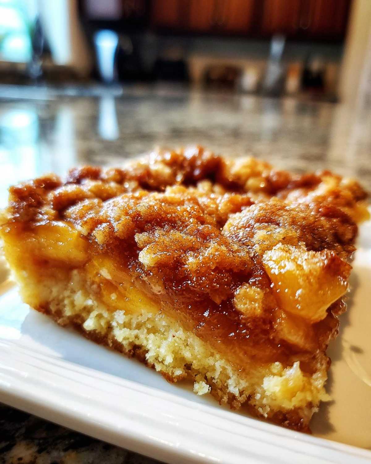 Close-up of a square slice of southern peach cobbler showing a moist cake base and a thick, gooey, cinnamon-sugar topping over peaches.