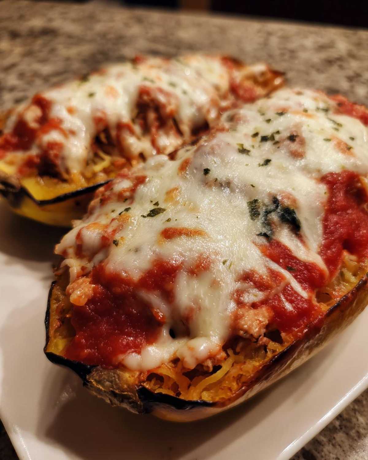 Two halves of baked spaghetti squash lasagna topped with rich marinara sauce and melted mozzarella cheese.