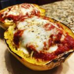 Close-up of baked spaghetti squash lasagna halves topped with melted mozzarella cheese and herbs.