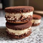 Two stacked chocolate tiramisu cookies filled with thick, creamy mascarpone filling, dusted with cocoa powder.