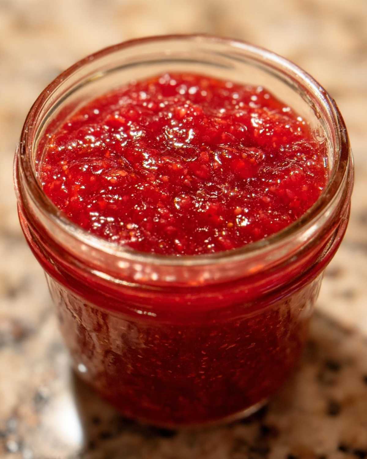 Close-up of bright red, chunky strawberry freezer jam filling a small glass jar.