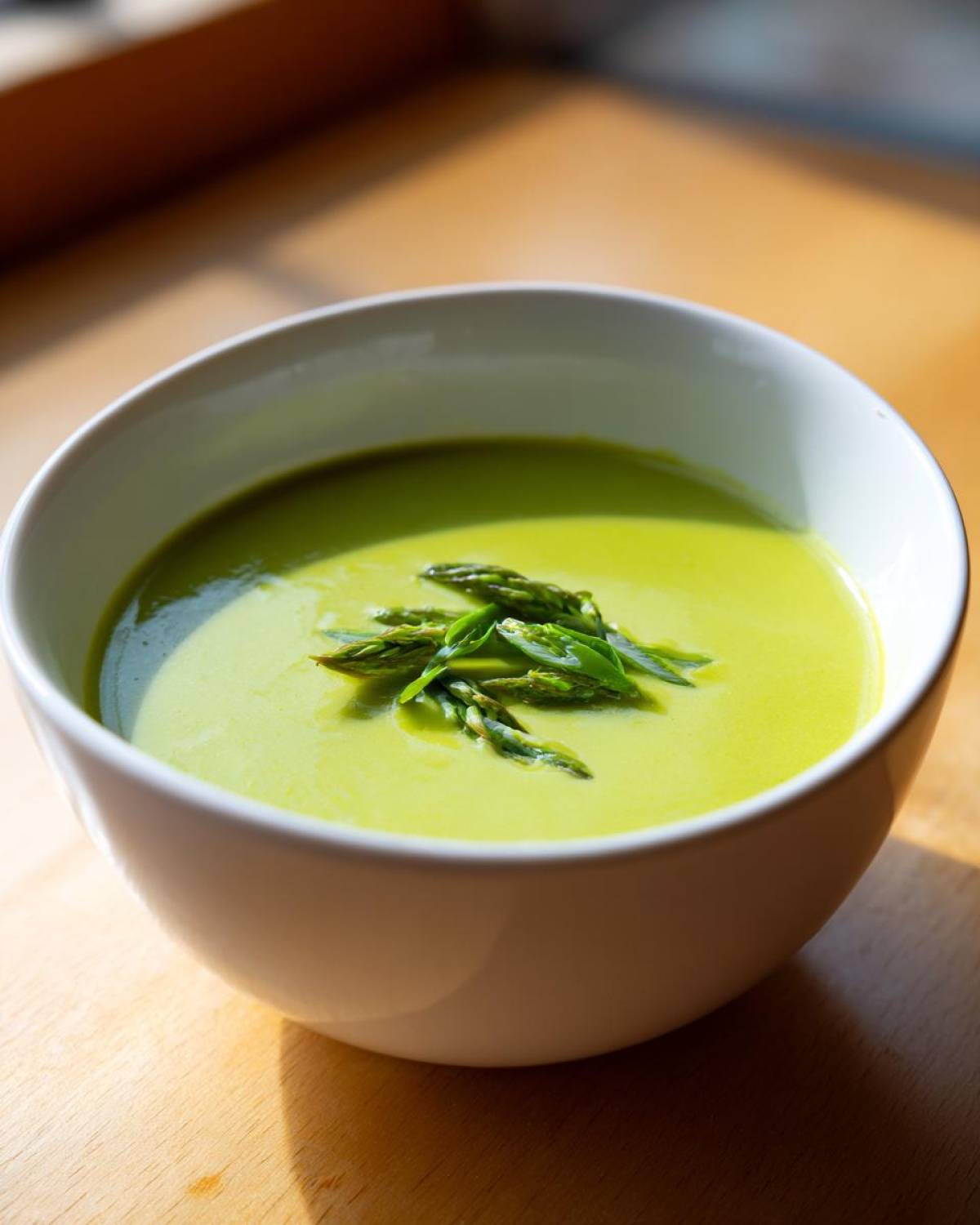 A close-up of bright green asparagus soup garnished with fresh asparagus tips in a white bowl.
