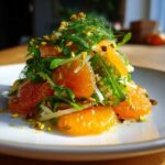 Close-up of a vibrant citrus salad featuring bright orange segments, arugula, fennel, and chopped pistachios.