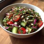 Close-up of a vibrant lentil salad featuring brown lentils, cucumber chunks, cherry tomatoes, red onion, and feta cheese.