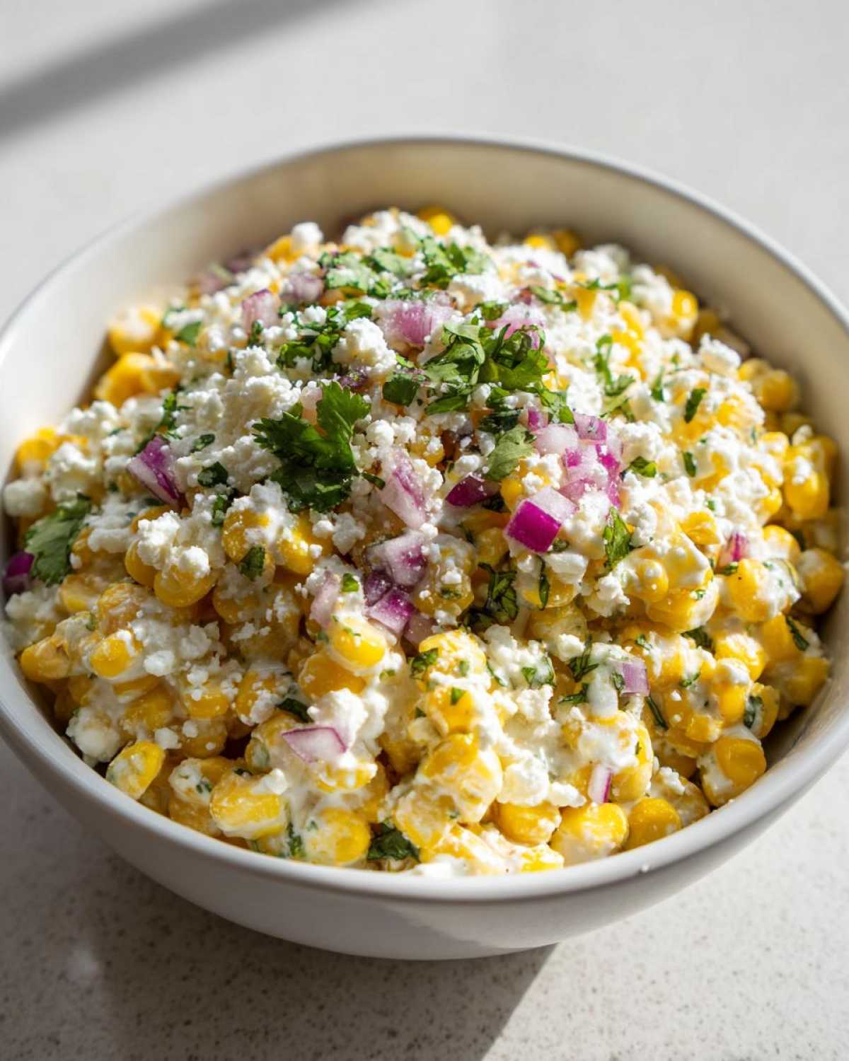 Close-up of a creamy street corn salad topped with crumbled white cheese, diced red onion, and fresh cilantro.
