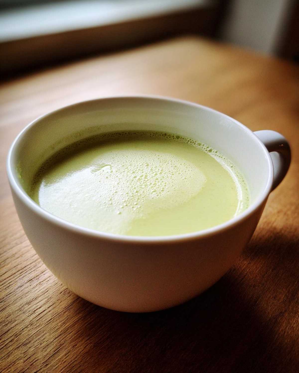 A close-up of a white mug filled with light green, frothy potato leek soup.