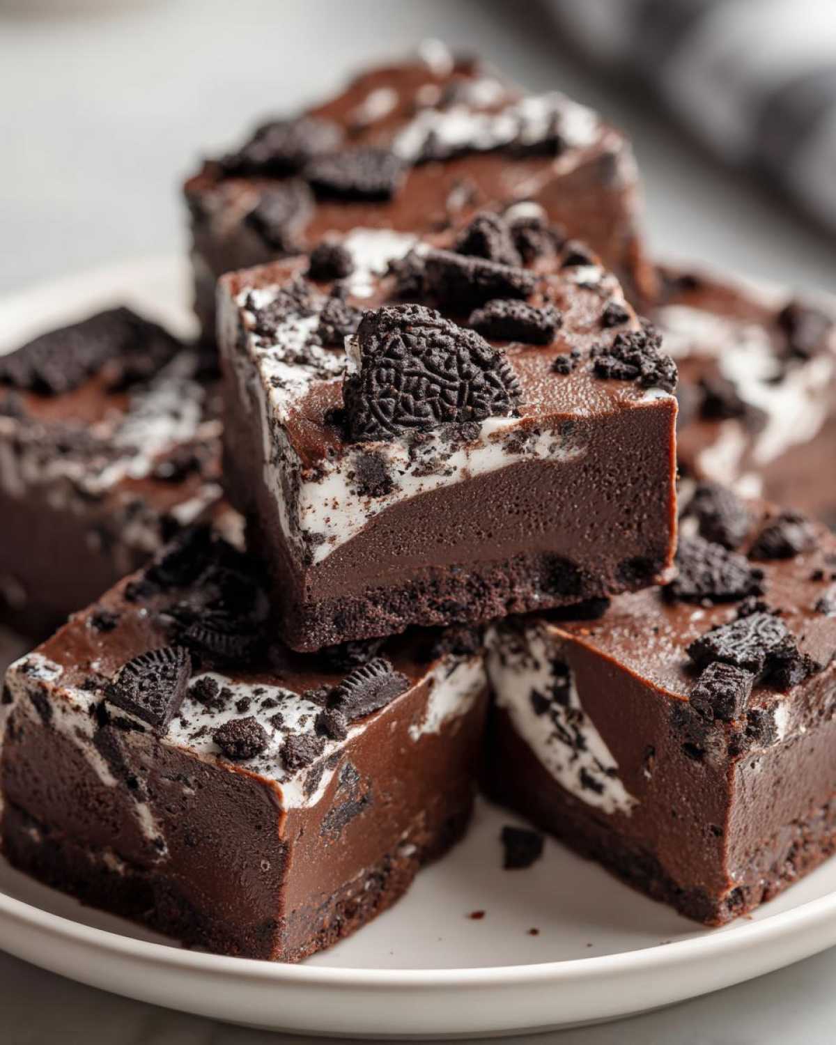 Close-up of stacked squares of rich, dark chocolate Oreo fudge topped with crushed cookies.