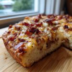 Close-up of a thick slice of bacon cheeseburger casserole with melted cheese and crispy bacon topping.