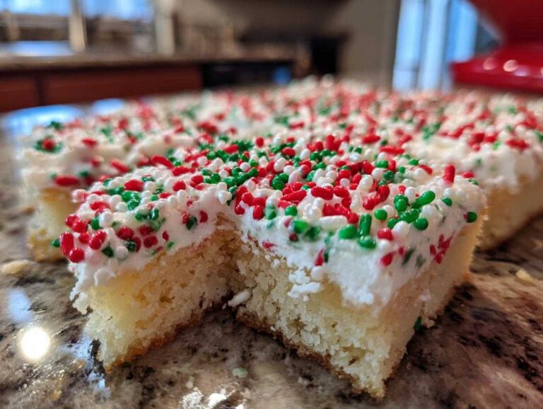 A close-up, low-angle shot of freshly cut christmas sugar cookie bars topped with white frosting and red, green, and white sprinkles.