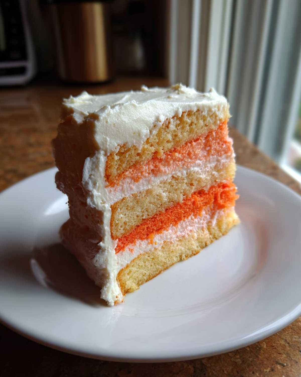 A tall slice of layered Creamsicle Cake featuring vanilla and orange layers with white frosting.