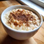 A close-up of a white bowl filled with creamy rice pudding recipe, generously dusted with cinnamon.