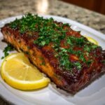 A perfectly cooked, glazed salmon recipe fillet topped with fresh chopped parsley and served with lemon slices.