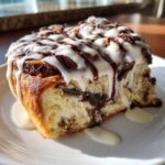 A close-up of a single, decadent Oreo cinnamon roll slice covered in white icing and dark chocolate drizzle.