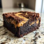 A rich, fudgy square of peanut butter swirl brownies sitting on a granite countertop.