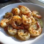 Close-up of perfectly cooked air fryer frozen shrimp seasoned with herbs and spices in a white bowl.