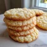 A close-up stack of four amazing soft sugar cookies with a crinkled, sugary texture, sitting on a white marble surface.