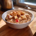 A close-up of a white bowl filled with creamy apple cinnamon oatmeal, topped with diced apples and cinnamon.