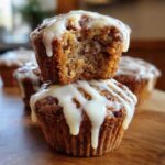 Two stacked cinnamon roll muffins, one with a bite taken out, drizzled with white icing.