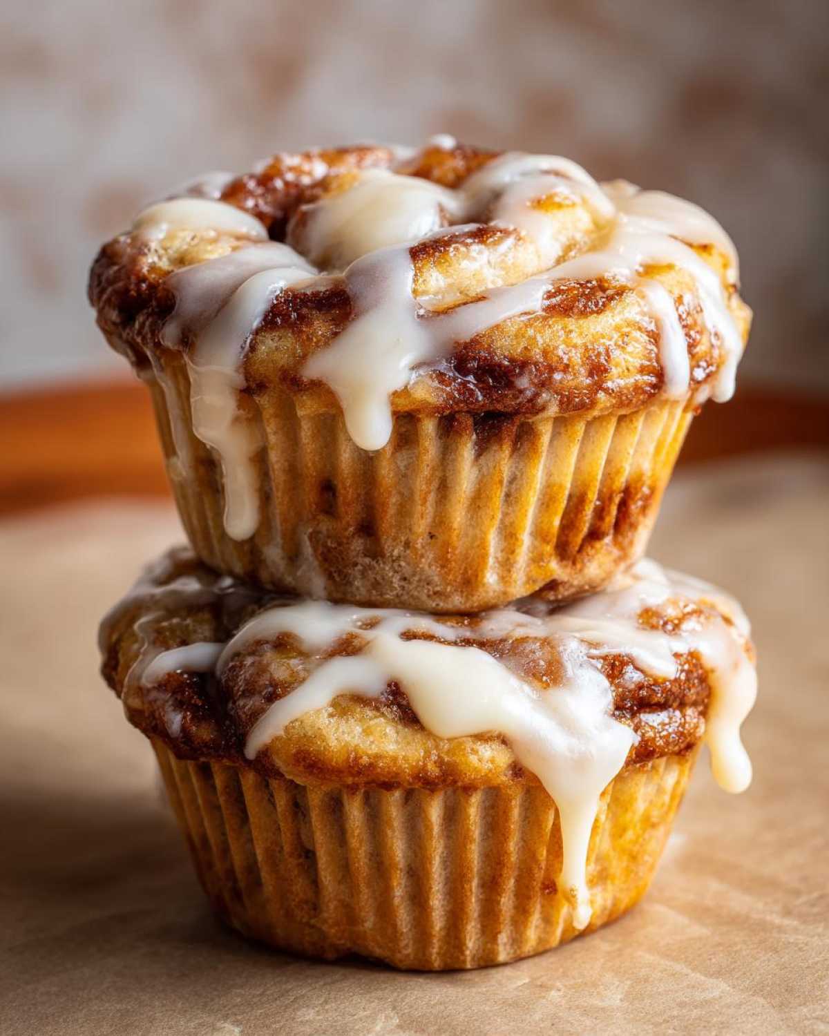 Two delicious cinnamon roll muffins stacked on top of each other, drizzled generously with white icing.