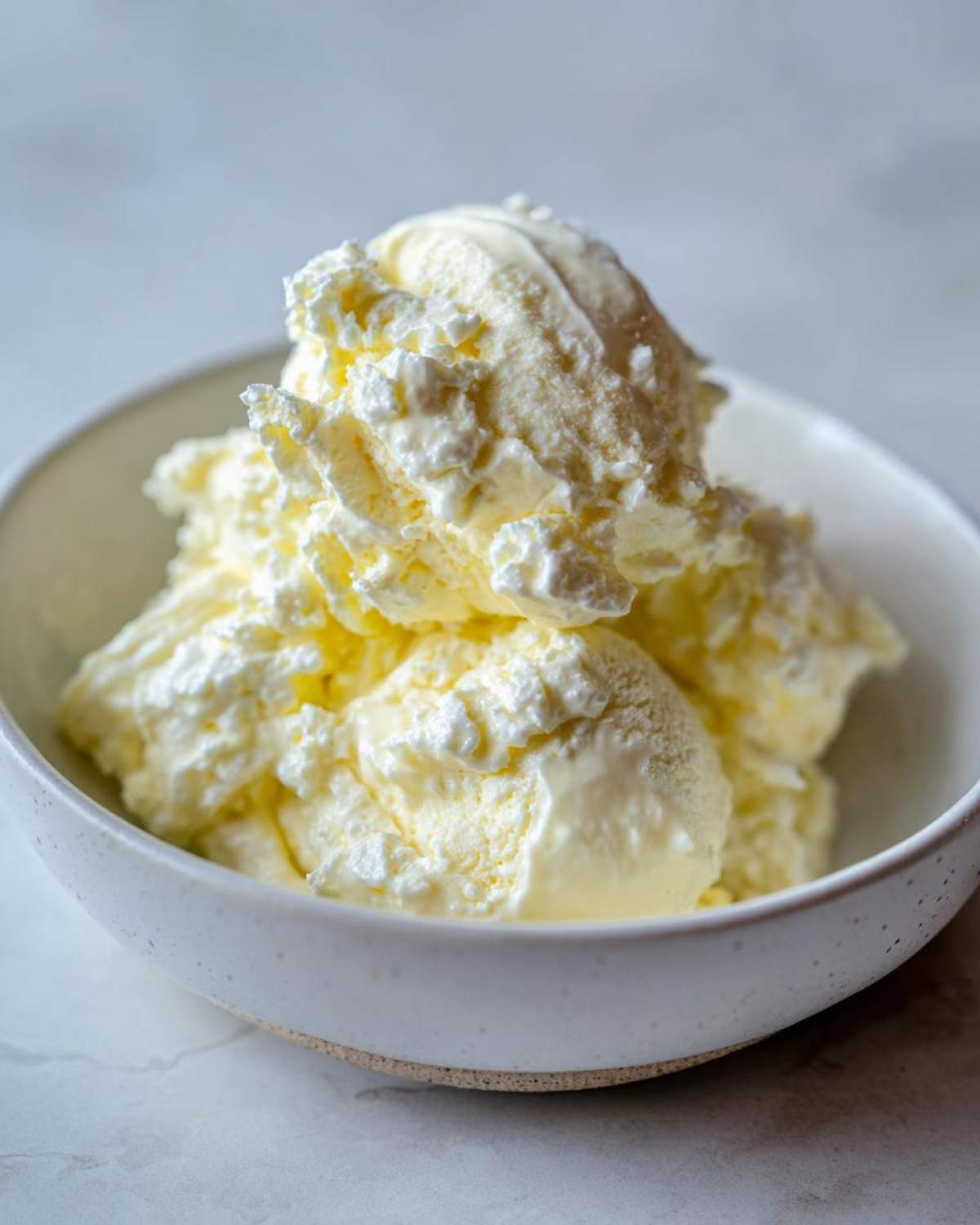 A close-up of a creamy, pale yellow mixture, resembling the base for an egg salad recipe, served in a speckled white bowl.