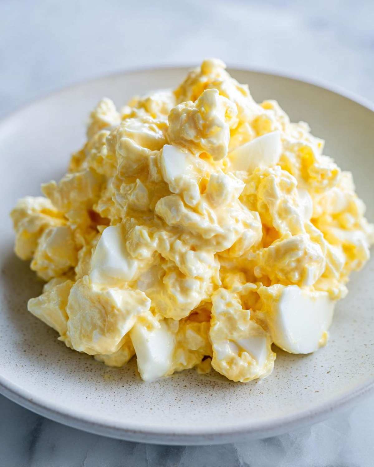 A close-up of a generous mound of creamy egg salad recipe, featuring chunky pieces of egg white and rich yellow yolk dressing.