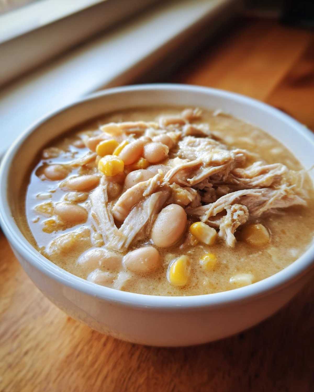 Close-up of creamy white chicken chili topped with shredded white chicken, navy beans, and corn kernels.