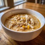 Close-up of a hearty bowl of creamy white chicken chili topped with shredded white chicken, corn, and beans.