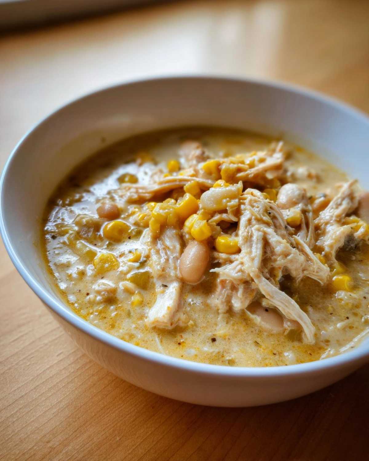 Close-up of a bowl filled with creamy white chicken chili, featuring shredded white chicken, corn, and beans.