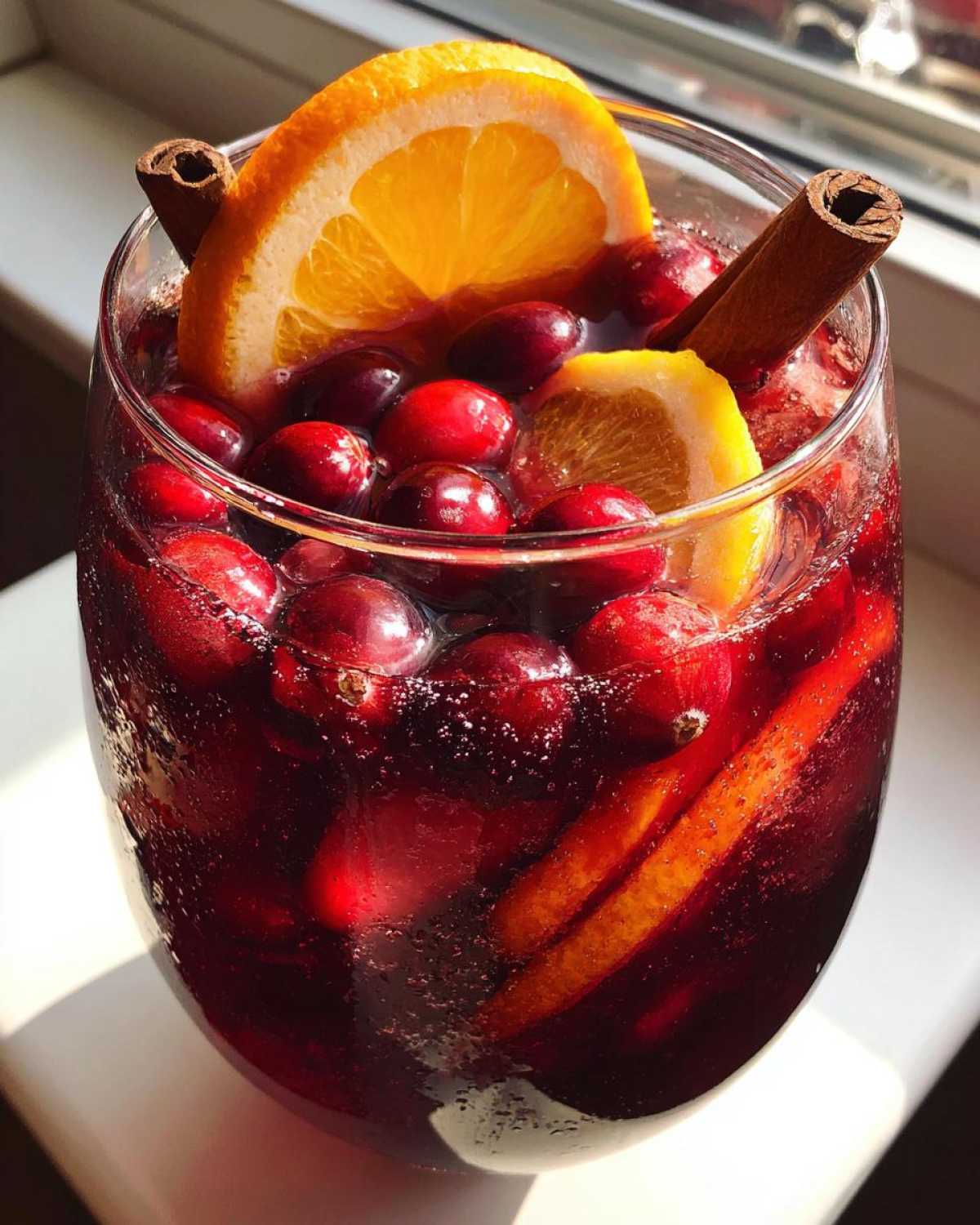 Close-up of a glass filled with rich red Christmas sangria, garnished with fresh cranberries, orange slices, and cinnamon sticks.