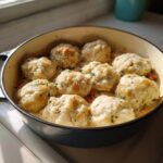 Close-up of fluffy, golden-brown dumplings sitting atop a creamy sauce in a cast iron pot, perfect for chicken and dumplings.