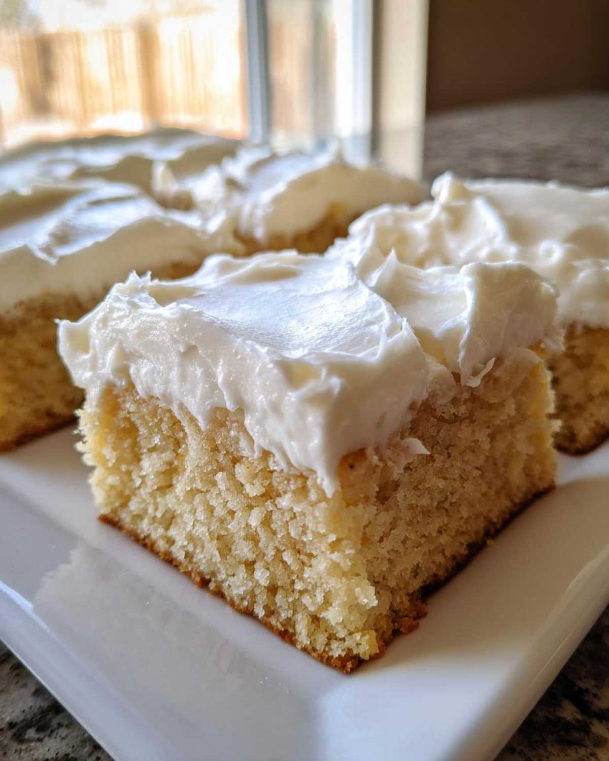 A close-up of a thick, square portion of soft sugar cookie bars topped with generous white frosting.