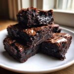 Close-up of a stack of five fudgy Oreo brownies with shiny, cracked tops served on a white plate.