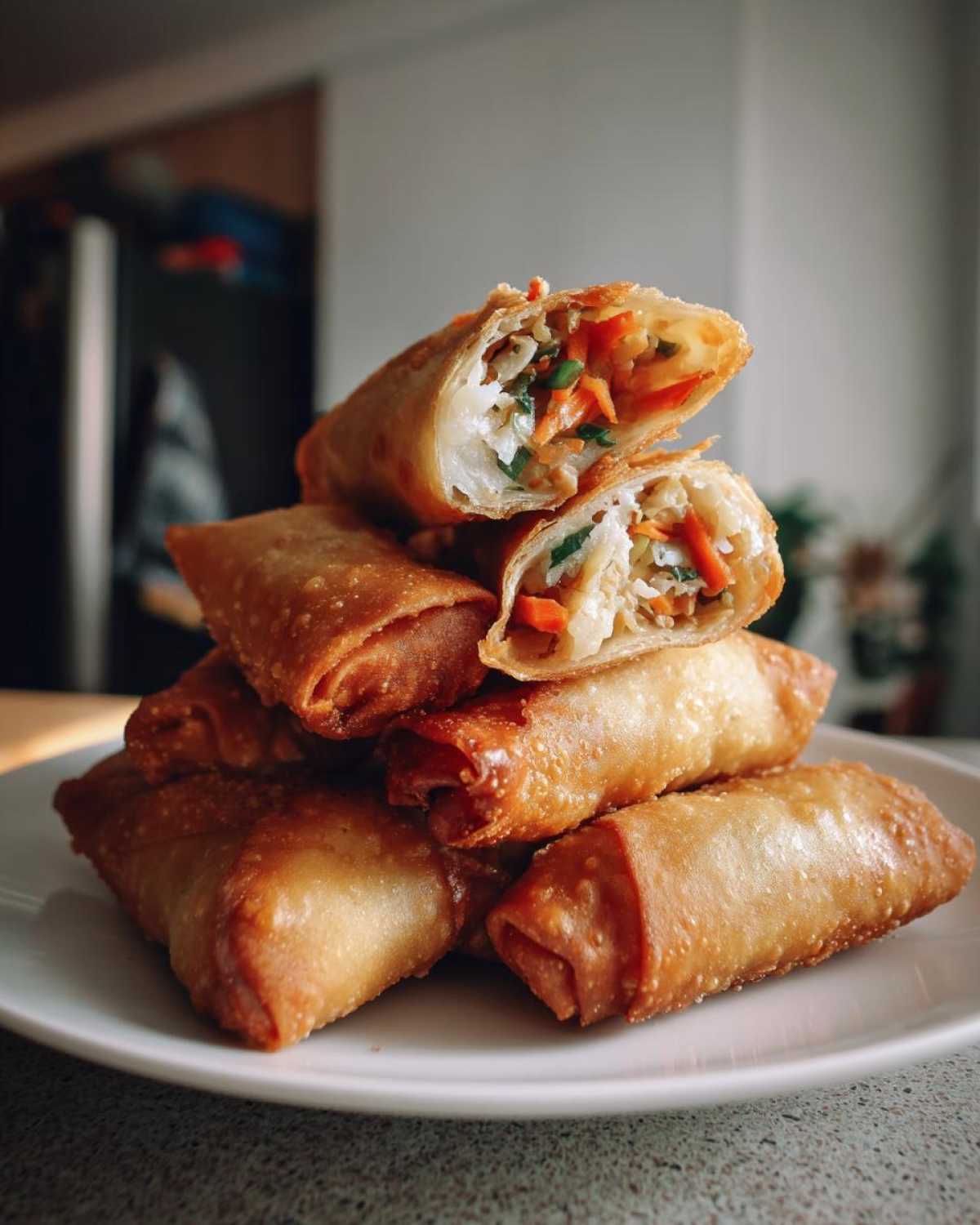 A stack of crispy, golden brown homemade egg roll appetizers, with the top two cut open to show the vegetable filling.