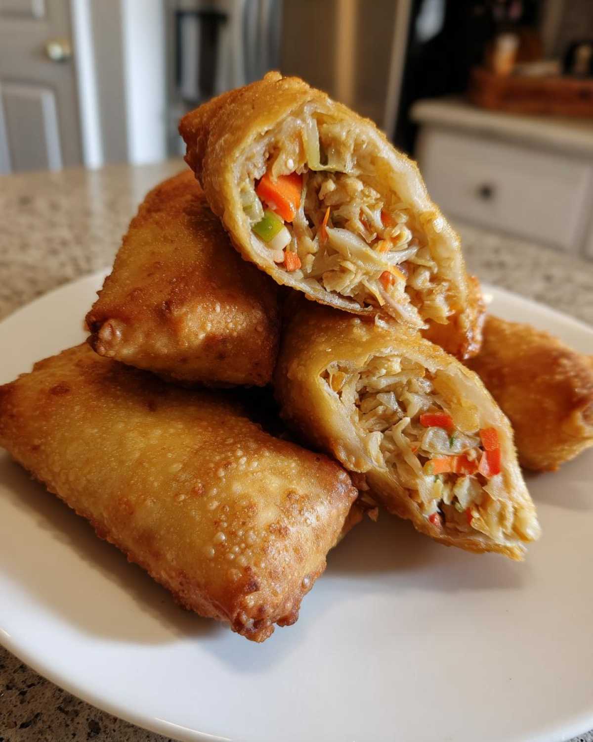 A stack of golden brown, crispy homemade egg roll pieces, one cut open revealing shredded cabbage and carrot filling.