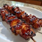 Close-up of two skewers loaded with juicy, caramelized, and slightly charred chicken skewers on a white plate.