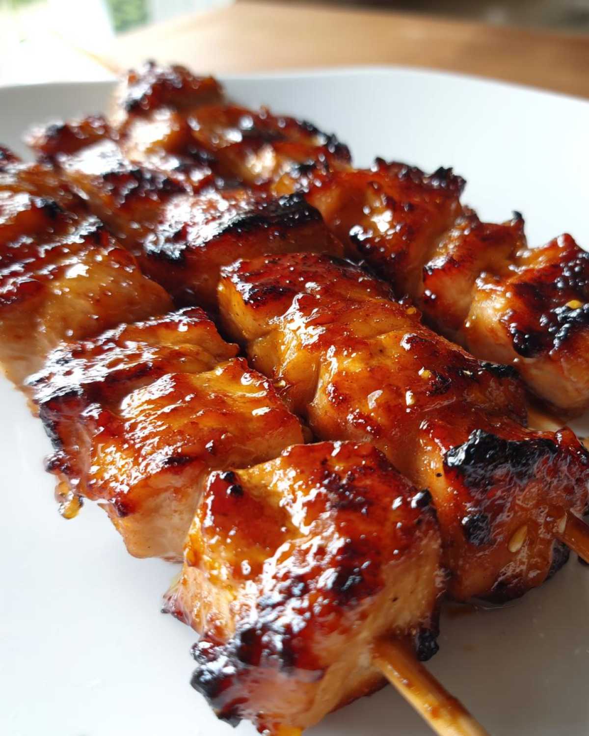 Close-up of several juicy, glazed chicken skewers with caramelized edges resting on a white plate.