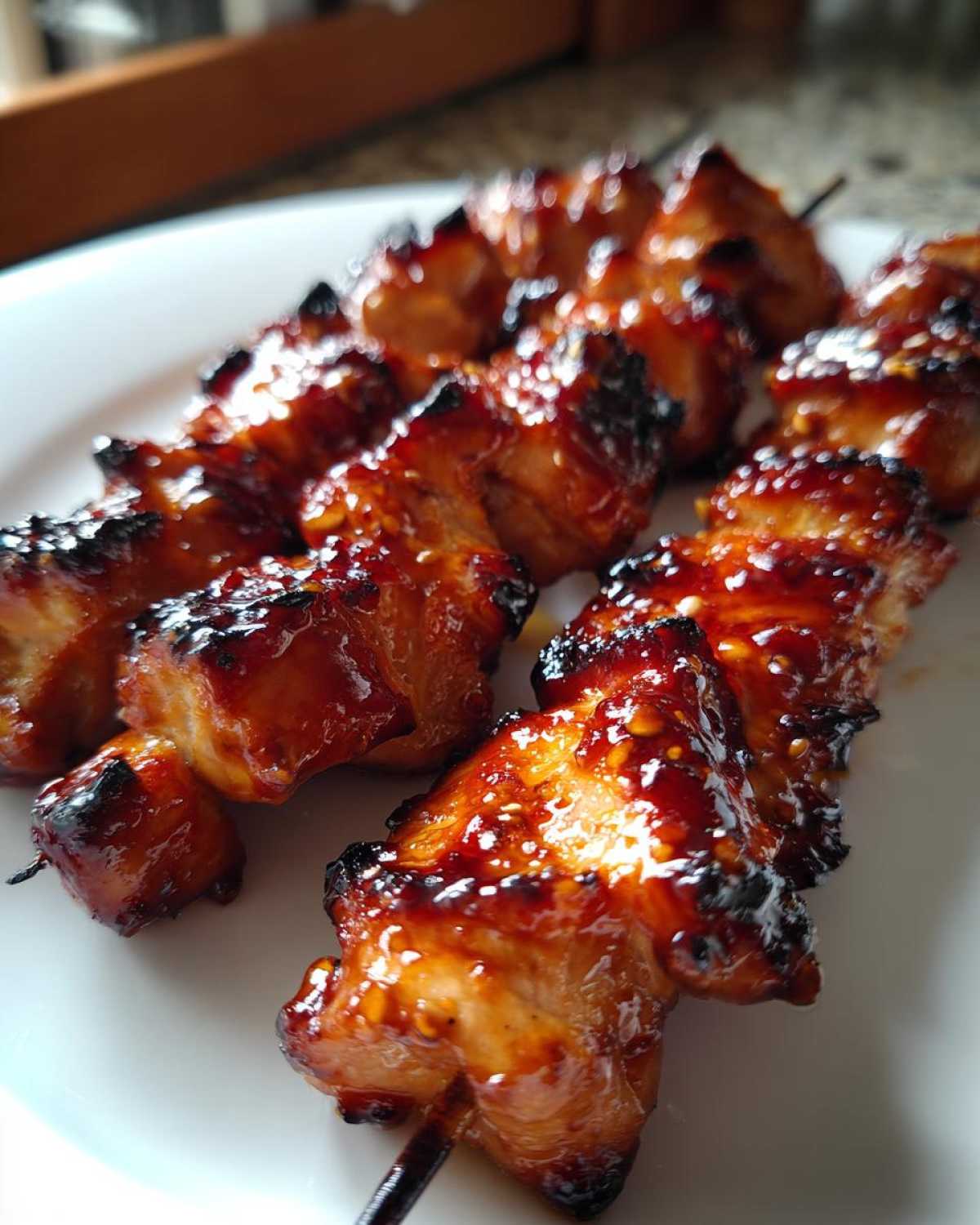 Close-up of several juicy, glazed chicken skewers resting on a white plate, showing caramelized edges.