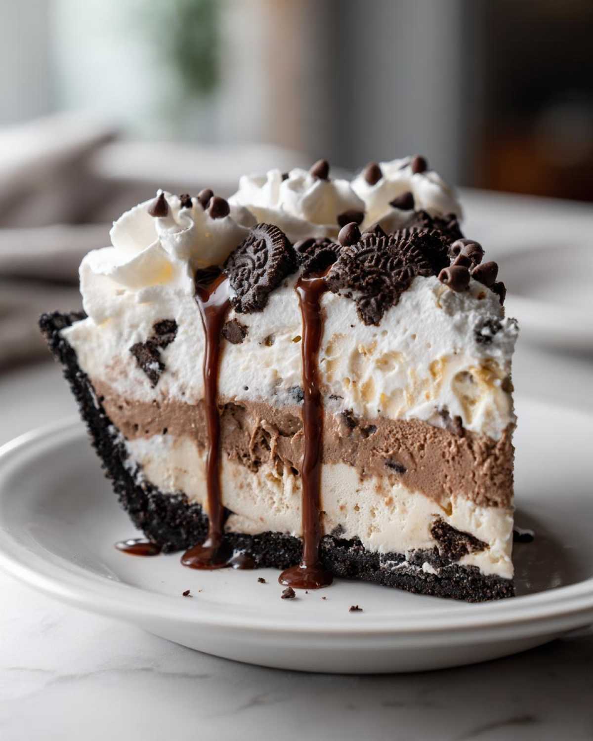 A tall slice of layered ice cream pie with a dark crust, vanilla and chocolate ice cream layers, topped with whipped cream and cookies.