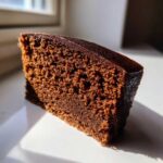 Close-up of a dense, dark brown slice of cake, likely gingerbread, showing its moist crumb texture.