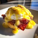Close-up of a delicious eggs benedict featuring a poached egg, crispy bacon, and rich hollandaise sauce.
