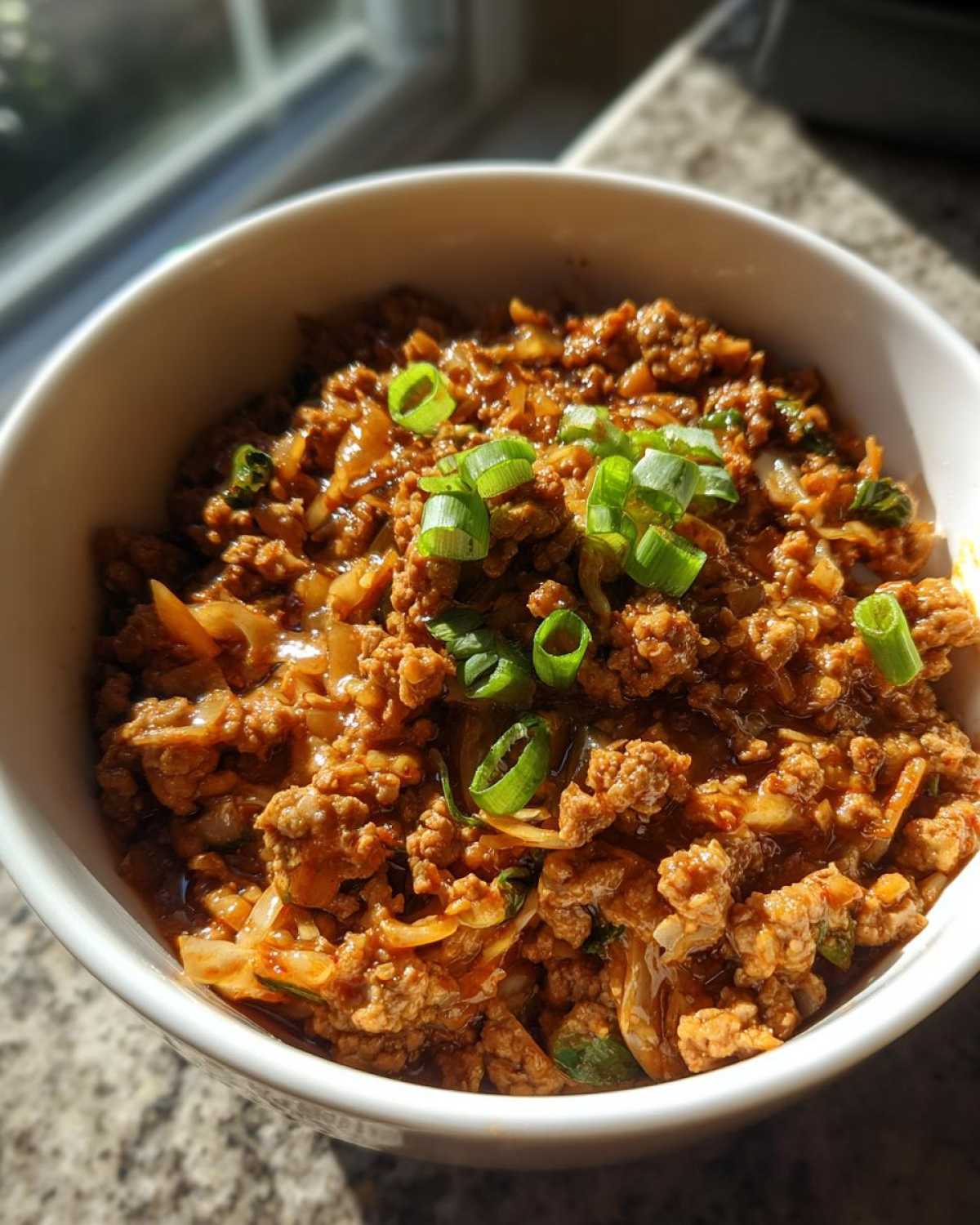 Close-up of a white bowl filled with savory egg roll in a bowl mixture, garnished with fresh green onions.