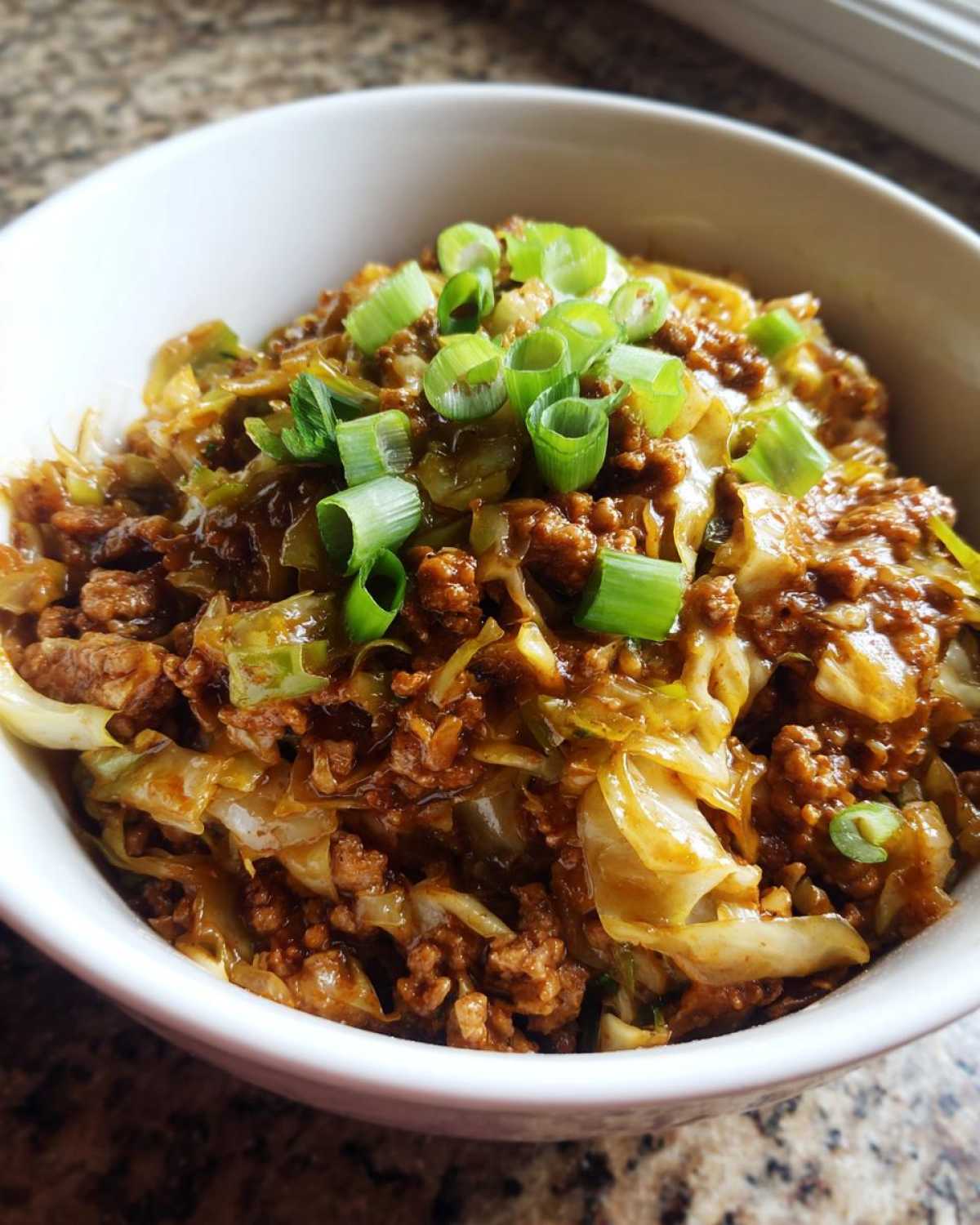 Close-up of a serving of savory egg roll in a bowl with ground meat and cabbage, garnished with fresh green onions.