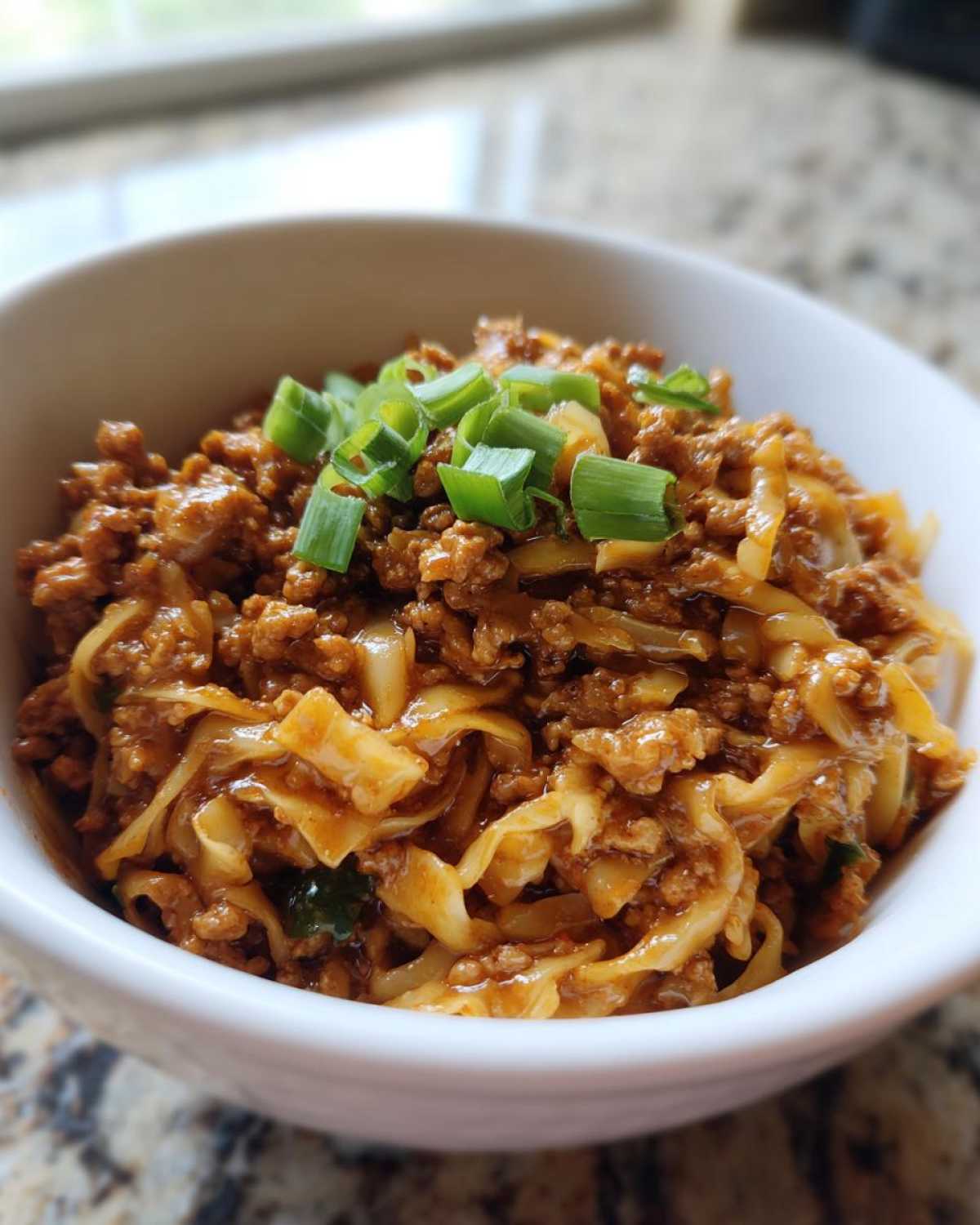 Close-up of a white bowl filled with savory egg roll in a bowl mixture, topped with sliced green onions.